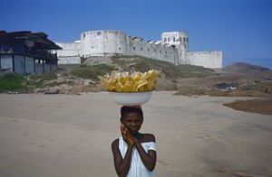 320px-Zicht_op_fort_vanaf_het_strand_met_meisje_met_bananenschaal_op_haar_hoofd_op_de_voorgrond_-_Cape_Coast_-_20373090_-_RCE.jpg